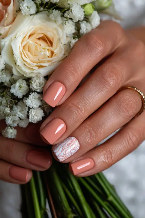 Bridal fingers lightly touching a bouquet stem, square nails in soft peach with one accent nail featuring a white swirl pattern and glossy finish 