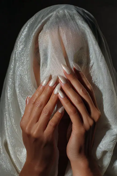 Bridal hand delicately lifting veil, sculpted almond-shaped acrylic nails in glossy ivory with fine gold glitter fade