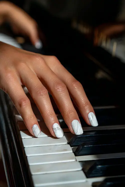 Bridal hand gently brushing over a piano key, showcasing square nails with translucent chrome base and white marble swirl details, classic indoor background 