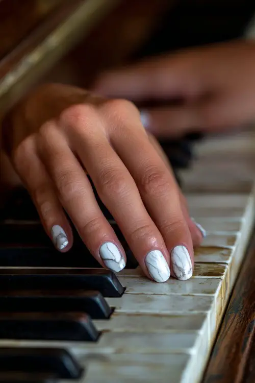Bridal hand gently brushing over a piano key, showcasing square nails with translucent chrome base and white marble swirl details, classic indoor background