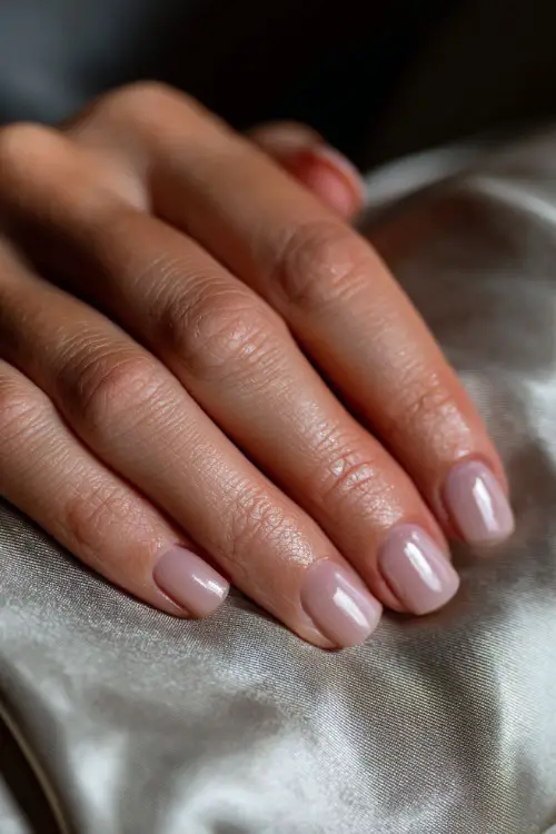 Bridal hand laying flat on a satin pillow, clean short square nails in light pink gloss with subtle silver dot along the center of each nail