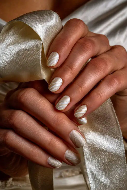 Bride’s fingers wrapped around satin ribbon, almond nails in creamy ivory with white swirl detailing and clear gloss overlay 