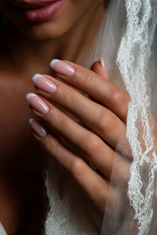 Bride’s hand adjusting her veil, showing elegant coffin-shaped nails with sheer pink base and white lace tips