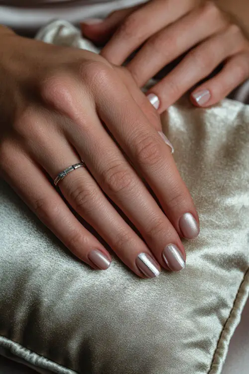 Bride’s hand beside a silk ring pillow, square nails in soft rose-beige polish with silver chrome striping on two accent nails