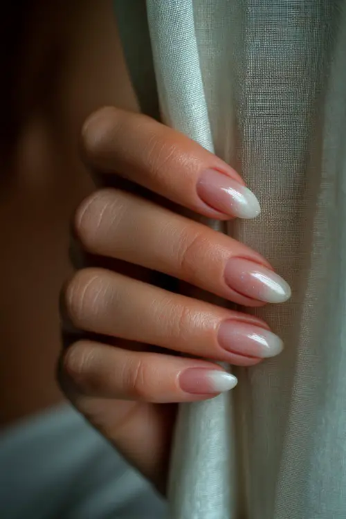 Bride’s hand brushing curtain aside, almond nails in sheer milky white with pink ombré tips and floral glitter accent 