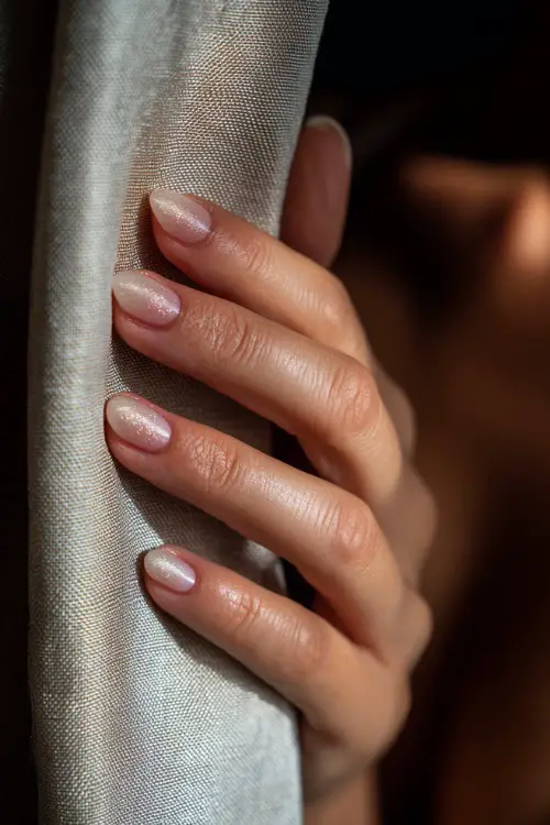 Bride’s hand brushing curtain aside, almond nails in sheer milky white with pink ombré tips and floral glitter accent 