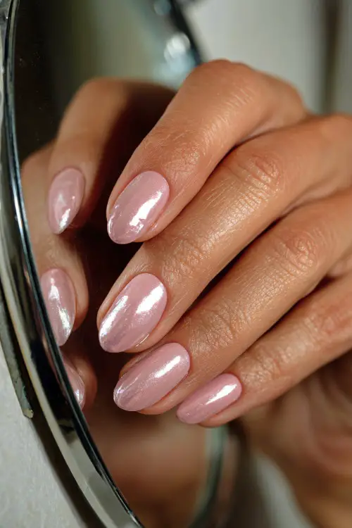 Bride’s hand brushing over mirror, short oval nails in glassy pastel pink with chrome shimmer tip on one nail, classic vanity background