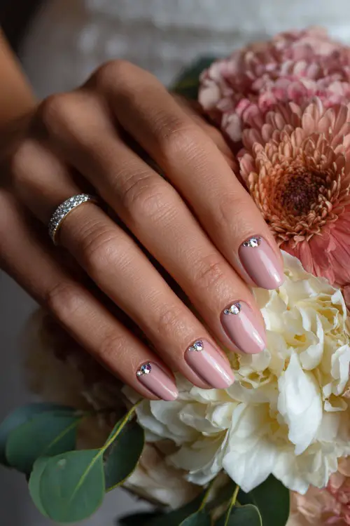 Bride’s hand curled around bouquet stem, soft almond nails in pastel mauve with a crystal bead crescent at the cuticle 