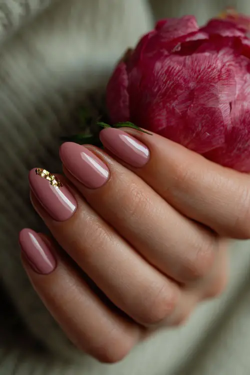 Bride’s hand delicately placing a pearl earring, showcasing almond nails in soft dusty rose with tiny gold leaf foil on one accent nail, moody romantic light