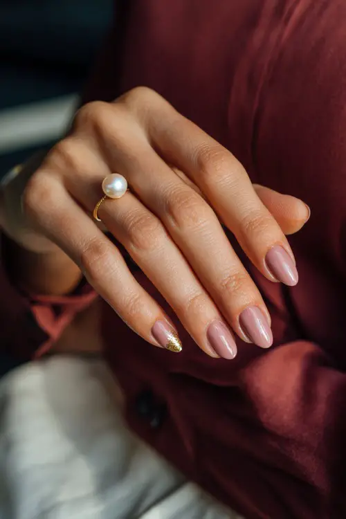 Bride’s hand delicately placing a pearl earring, showcasing almond nails in soft dusty rose with tiny gold leaf foil on one accent nail, moody romantic light