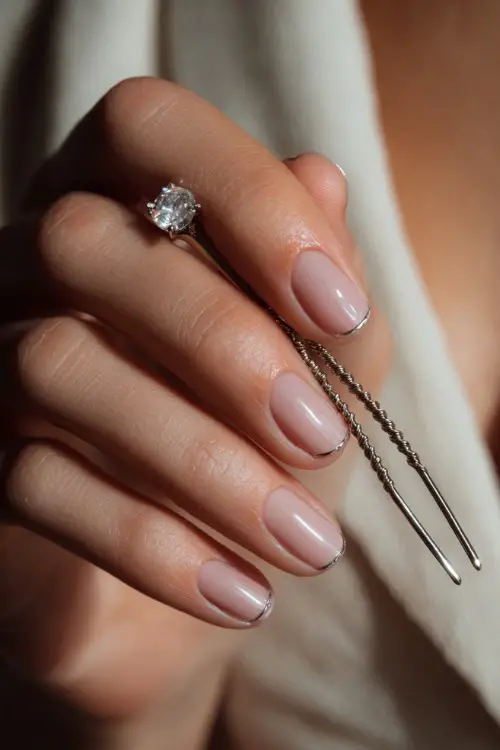 Bride’s hand delicately touching a crystal hairpin, showcasing tapered square nails in classic pale pink with a silver chrome French tip
