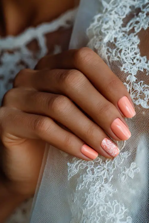 Bride’s hand delicately touching veil, short natural-shaped nails in soft pastel peach with one accent nail featuring floral stamping 