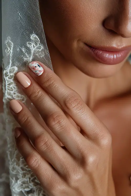 Bride’s hand delicately touching veil, short natural-shaped nails in soft pastel peach with one accent nail featuring floral stamping