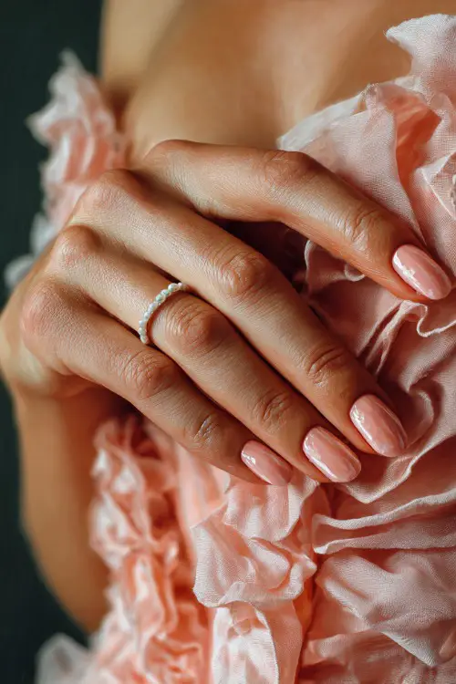 Bride’s hand gently brushing chiffon gown, soft peach oval nails with shimmer topcoat and micro pearl detail on the ring finger 