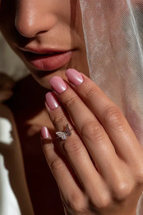 Bride’s hand gently lifting her veil, soft baby pink nails with chrome shimmer and subtle butterfly charm on the index finger