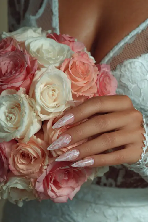 Bride’s hand over bouquet of soft roses, long stiletto acrylic nails with a translucent base and white lace detailing 