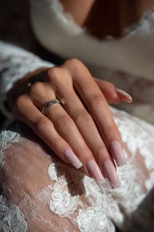 Bride’s hand over sheer lace, long coffin acrylic nails with pastel pink base and rhinestone-encrusted cuticles, luxury indoor lighting