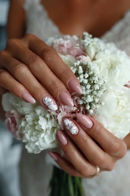 Bride’s hand over soft bouquet, almond nails painted pale pink with white floral stamping and clear crystal details