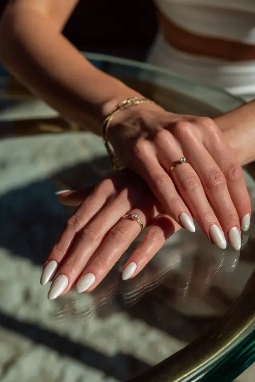 Bride’s hand resting gently on a glass table, showcasing stiletto nails in matte ivory with minimal pearl drop charm on each ring finger