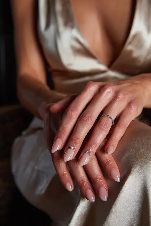 Bride’s hand resting on her lap, almond-shaped nails in sheer champagne pink with a crystal-studded crescent on two accent fingers 