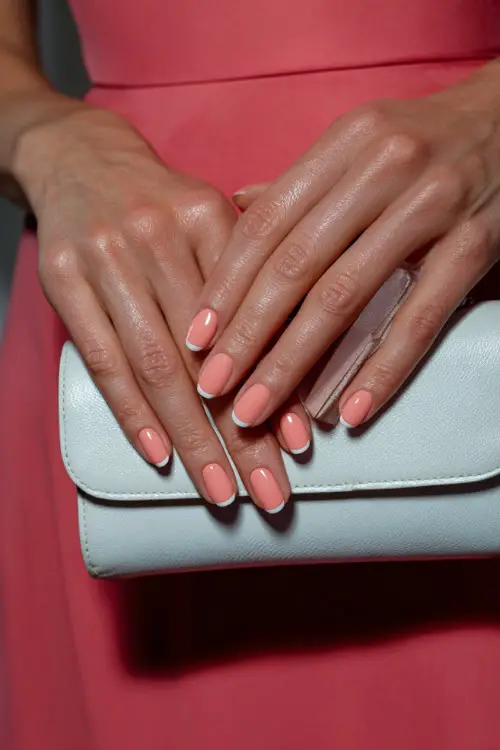 Bridesmaid’s fingers curled around a pastel clutch, ballerina-shaped nails in pale coral with diagonal white tips and glossy topcoat 