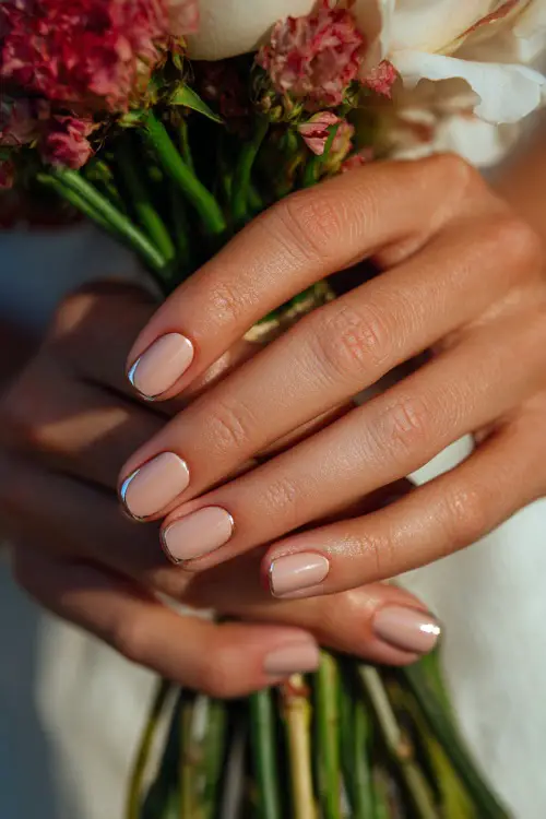 Bridesmaid’s fingers interlaced with bouquet stem, light caramel polish with chrome half-moon cuticle detail 