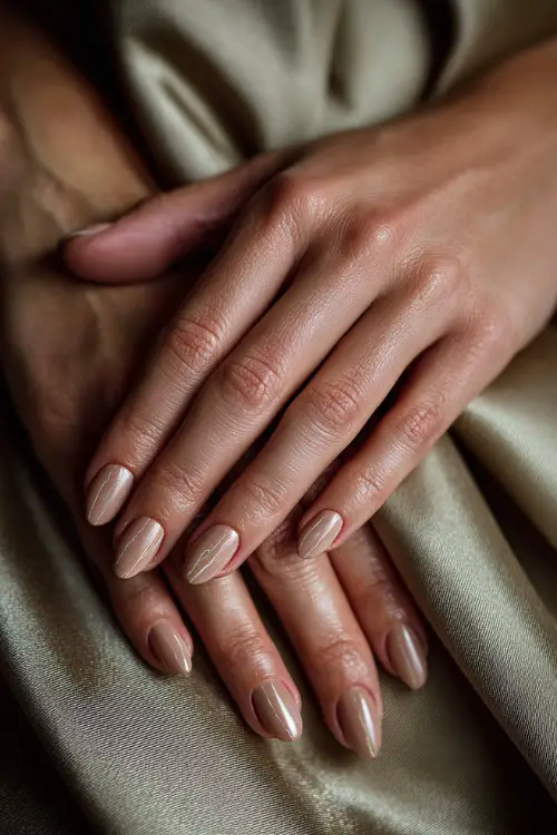Bridesmaid’s fingers resting on satin fabric, almond-shaped nails in pale beige with fine gold striping and glossy overlay