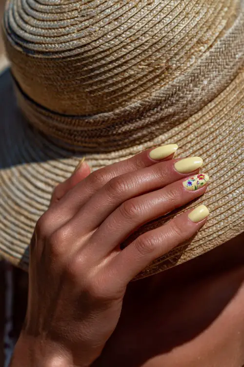 Bridesmaid’s hand adjusting her sunhat, short ballerina nails in pastel yellow with glossy finish and tiny floral decals on two fingers 