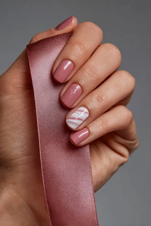 Bridesmaid’s hand against a soft chiffon ribbon, short ballerina nails in warm dusty rose with one nail in transparent white swirl design 