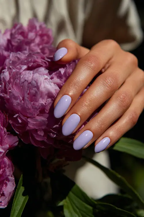Bridesmaid’s hand arranging flowers, oval nails painted pastel lilac with subtle pearl shimmer and single white dot detail on each finger 