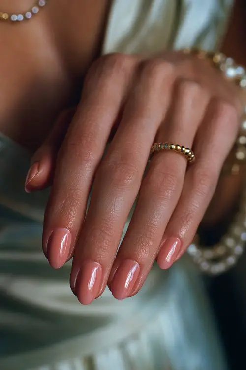 Bridesmaid’s hand gently holding a wedding program, almond nails in pastel peach with glossy finish and small gold beads forming a delicate curve at the base 