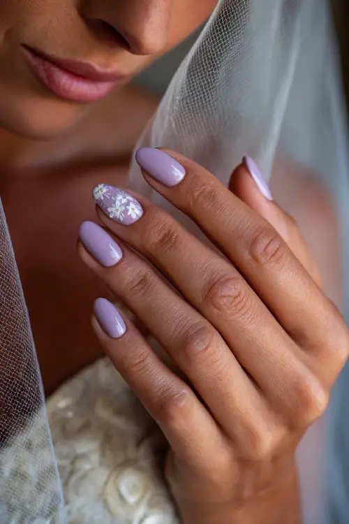 Bridesmaid’s hand softly brushing against veil, almond nails in pale lavender with a matte finish and white floral stamp art on one accent nail 