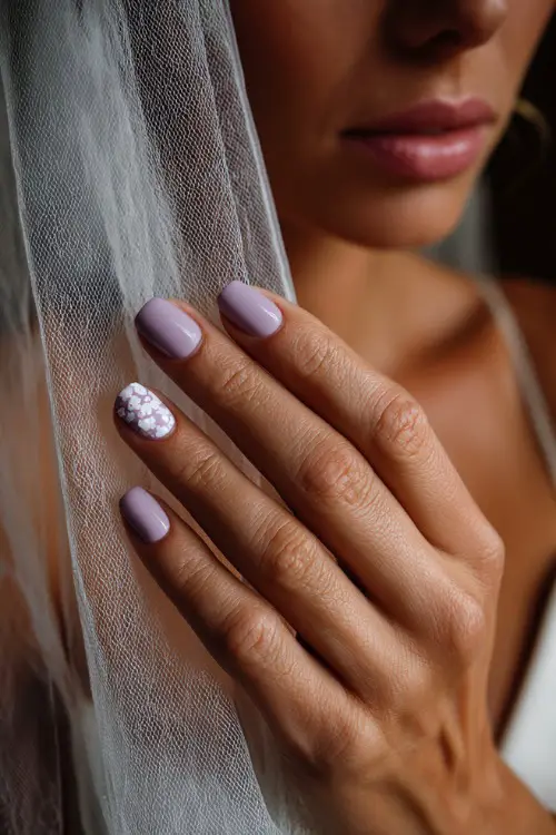 Bridesmaid’s hand softly brushing against veil, almond nails in pale lavender with a matte finish and white floral stamp art on one accent nail