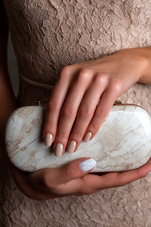Bridesmaid’s hand softly placed on a lace clutch, short oval nails in milky beige with fine white marble detailing on two accent fingers