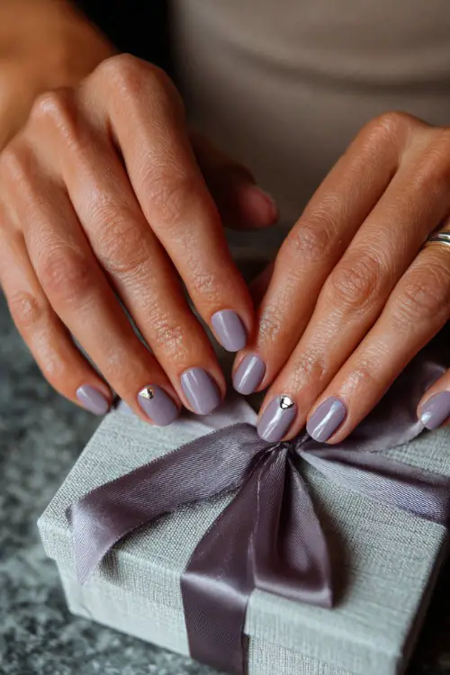 Bridesmaid’s hand tying a bow on a favor box, short rounded nails in muted lavender with silver half-moon detail at the cuticle 