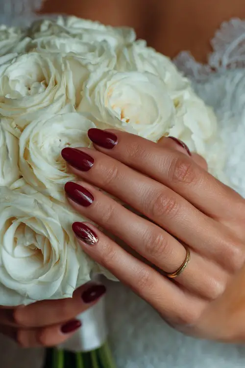 Close-up of a bride’s hand gently holding a white rose bouquet, long almond-shaped nails painted in deep ruby red with a high-gloss finish