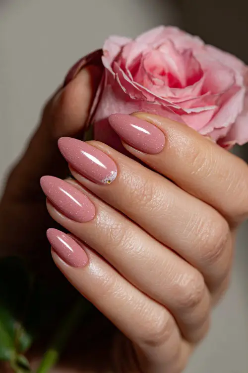 Close-up of a hand holding a soft pink rose, almond-shaped nails in sheer pastel pink with glossy finish and tiny white daisies on two fingers 