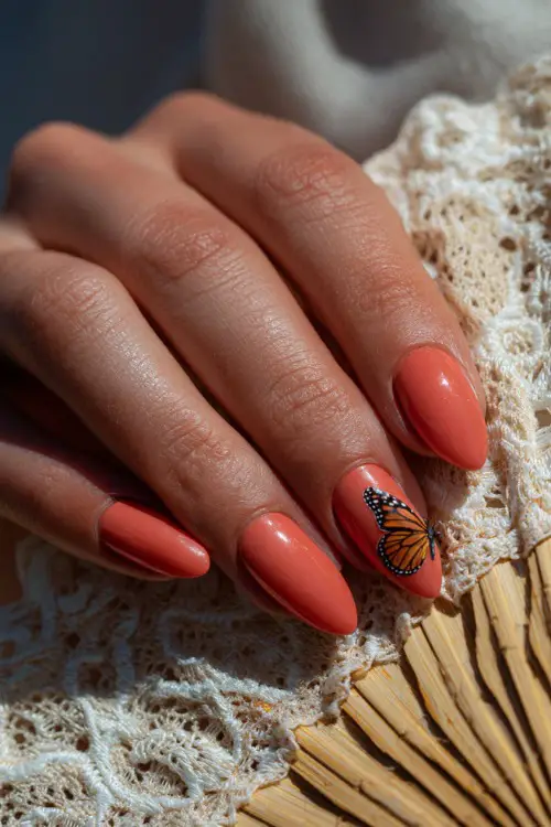Close-up of a hand resting on a lace fan, almond-shaped nails in pastel coral with a single butterfly decal on the middle finger 