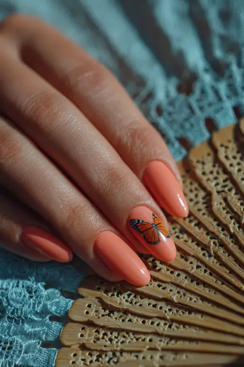 Close-up of a hand resting on a lace fan, almond-shaped nails in pastel coral with a single butterfly decal on the middle finger