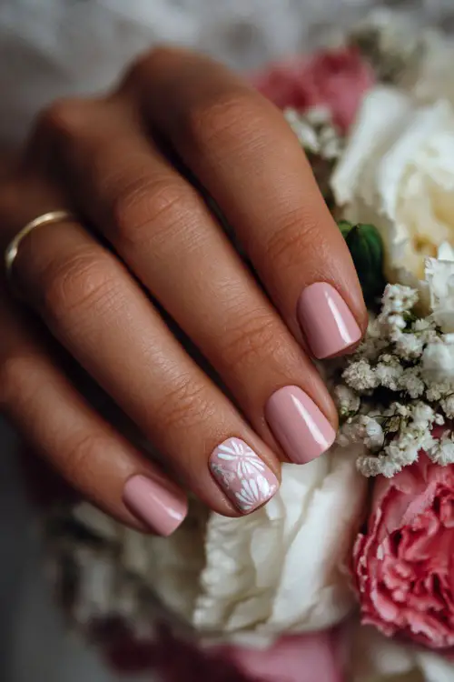 Close-up of bridal hand beside soft floral décor, short square nails in matte pastel pink with delicate white line art on one nail 