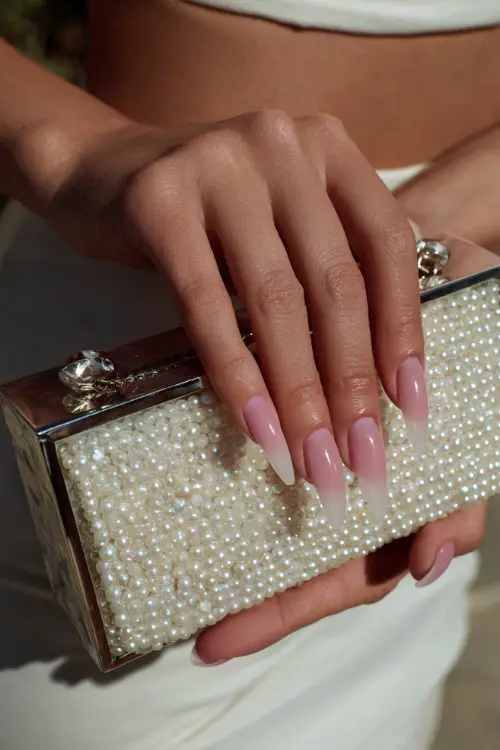 Close-up of bride’s hand holding a pearl clutch, long coffin-shaped acrylic nails with soft pink ombré and clear tips 