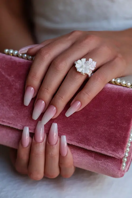 Close-up of bride’s hand holding a pearl clutch, long coffin-shaped acrylic nails with soft pink ombré and clear tips