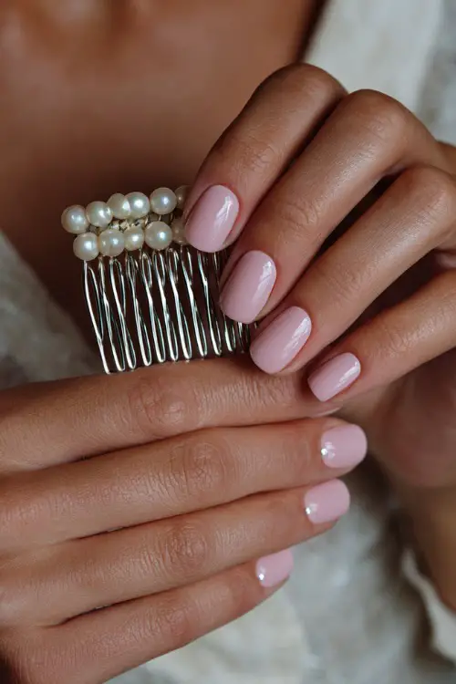 Close-up of bride’s hand holding a pearl hair comb, short square nails in soft pink with glossy finish and silver dot accents near the cuticle 