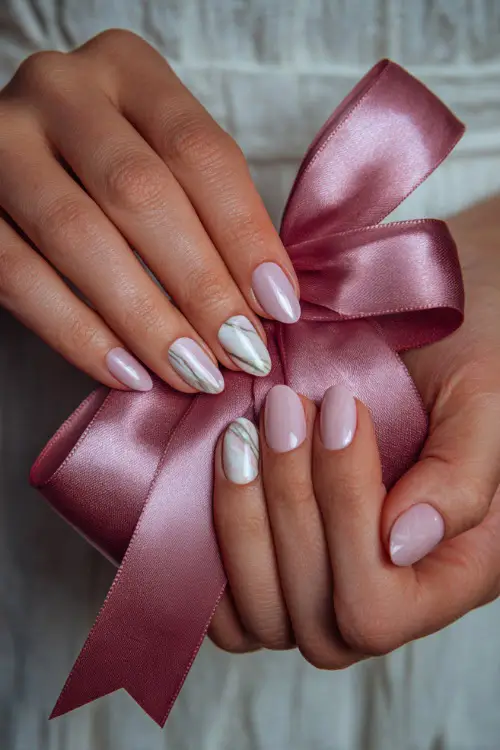 Close-up of bride’s hand holding a satin ribbon, almond-shaped nails in milky pink with white marble swirl on two fingers and shimmer overlay 