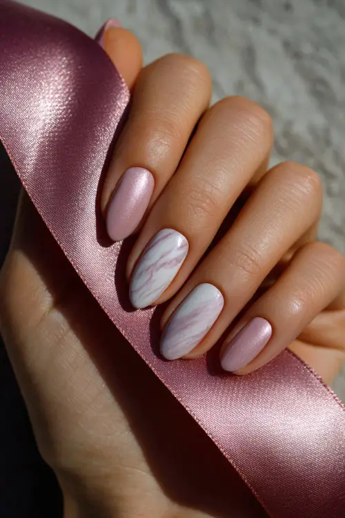 Close-up of bride’s hand holding a satin ribbon, almond-shaped nails in milky pink with white marble swirl on two fingers and shimmer overlay