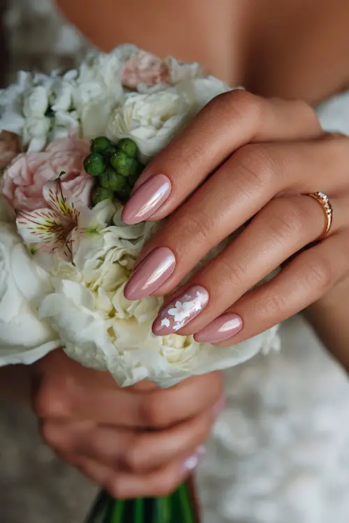 Close-up of bride’s hand holding a summer bouquet, almond-shaped nails in sheer blush pink with glossy finish and delicate white floral decals 