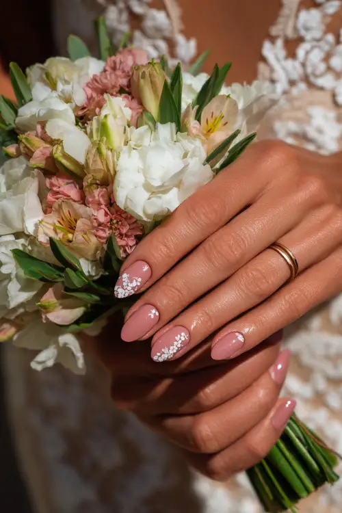 Close-up of bride’s hand holding a summer bouquet, almond-shaped nails in sheer blush pink with glossy finish and delicate white floral decals 