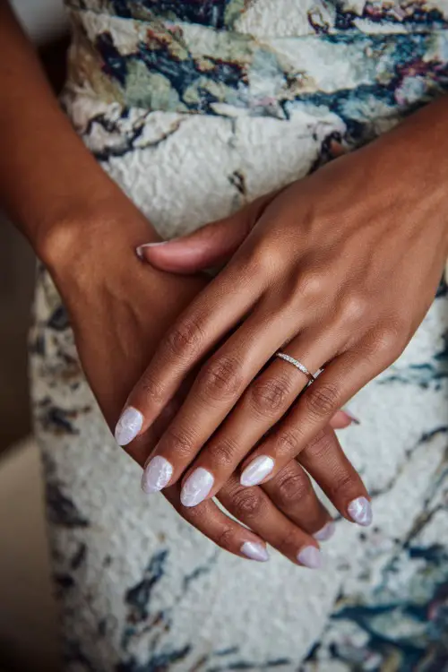 Close-up of bride’s hand holding handwritten vows, short oval nails in pastel lilac with marble swirl and pearl finish