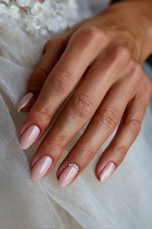 Close-up of bride’s hand on soft white tulle, ballerina nails in creamy pink with chrome shimmer overlay and tiny rhinestones forming a crescent near the cuticle 