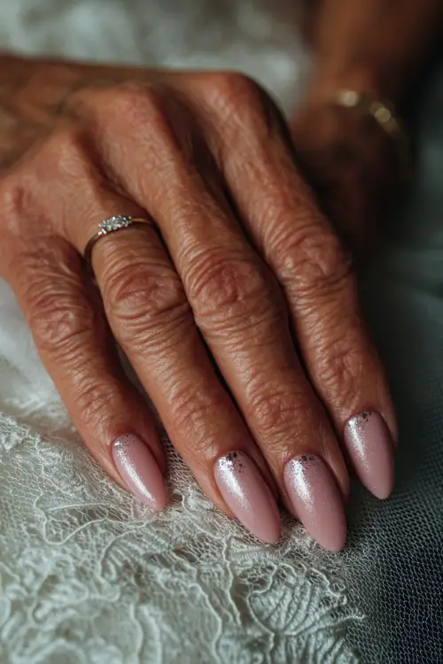 Close-up of bride’s hand resting on a lace veil, almond-shaped nails in soft blush pink with glossy finish and silver foil flakes on two accent fingers 